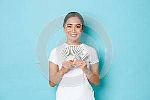 Shopping, money and finance concept. Smiling lucky asian female holding money and looking satisfied, winning lottery