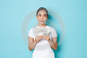 Shopping, money and finance concept. Thoughtful and creative pretty asian girl thinking where invest money, holding cash