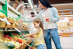 Daily Shopping. Mother and daughter in the supermarket choosing vegetables concentrated