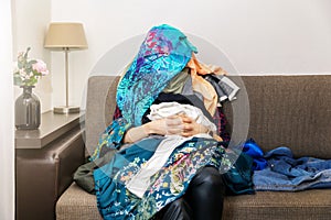 Shopping obsessed woman sitting on couch with clothes heap on her photo