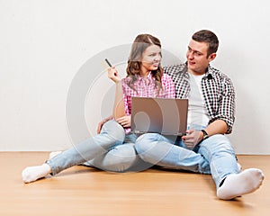 Shopping online together. Beautiful young loving couple shopping online while sitting on the floore together