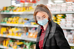 Shopping. Portrait of a young woman in a medical mask choosing products in a supermarket. The concept of shopping and the new
