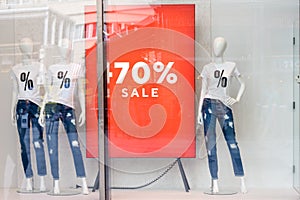 Shopping sale window display with mannequins wearing t-shirts with sign of Sale. Dummies in the store. Sale and fashion