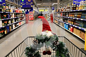 Shopping in shop, New Year sale, alcohol department for party, Funny Christmas gnome, wreath on supermarket trolley. Shopping cart