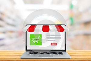 Shopping shop store  and shopping cart icon on laptop screen with blurry image of supermarket in background.