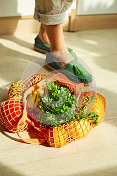 Shopping string grocery reusable mesh bag full of fresh fruits and vegetables on the floor at home