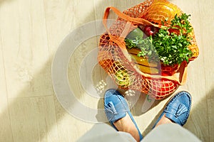 Shopping string grocery reusable mesh bag full of fresh fruits and vegetables on the floor at home