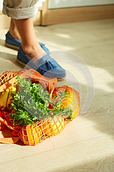 Shopping string grocery reusable mesh bag full of fresh fruits and vegetables on the floor at home