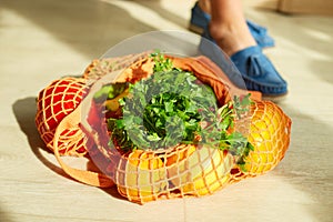 Shopping string grocery reusable mesh bag full of fresh fruits and vegetables on the floor at home