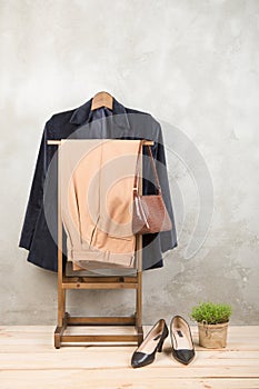 Shopping and style concept - clothes rack with trendy blue jacket and pants, bag and shoes on wooden floor and grey concrete