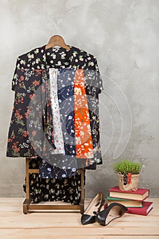 Shopping and style concept - clothes rack with trendy dresses in floral print, shoes and books on wooden floor and grey concrete