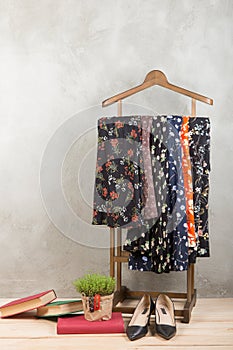 Shopping and style concept - clothes rack with trendy dresses in floral print, shoes and books on wooden floor and grey concrete