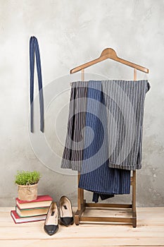 Shopping and style concept - clothes rack with trendy striped pants, books and shoes on wooden floor and grey concrete background