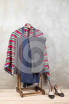 Shopping and style concept - clothes rack with trendy striped pants and plaid, shoes on wooden floor and grey concrete background