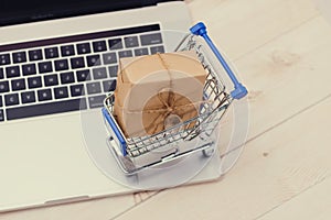 Shopping time. A laptop and shopping cart gift box wrapped with paper kraft on table