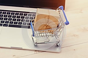 Shopping time. A laptop and shopping cart gift box wrapped with paper kraft on table