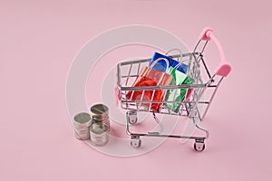 Shopping in trolley with bags on a pink background. Trolley cart and colorful paper shopping bags