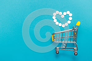 Shopping trolley cart with assorted medicine pills one blue background. Creative idea for drugstore, online pharmacy, health