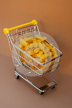 Shopping trolley cart Filled With Pasta on Beige background. Copy space for your text. Food and groceries shopping price