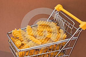 Shopping trolley cart Filled With Pasta on Beige background. Copy space for your text. Food and groceries shopping price