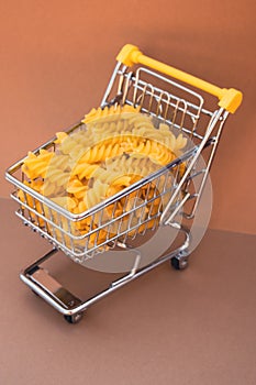 Shopping trolley cart Filled With Pasta on Beige background. Copy space for your text. Food and groceries shopping price