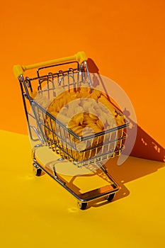 Shopping trolley cart Filled With Pasta on colorful yellow orange isometric background. Copy space for your text. Food