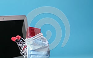 Shopping trolley or cart wrapped with medical face mask and computer screen at the background