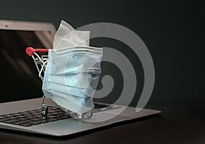 Shopping trolley or cart wrapped with medical face mask stand on top of computer laptop