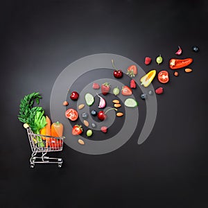 Shopping trolley filled with fresh organic vegetables, fruits and berries on black chalkboard. Square crop. Top view