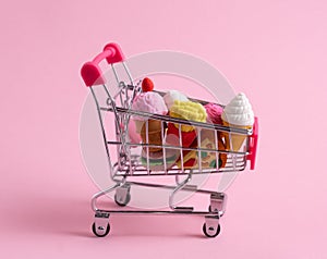 Shopping trolley full of sweets and fast food on pink background