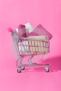 Shopping trolley full of wrapped gifts on pink background