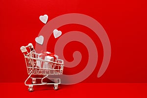 Shopping trolley with gift box, white love hearts on red background. St. Valentine\'s Day shopping and sale. copy space
