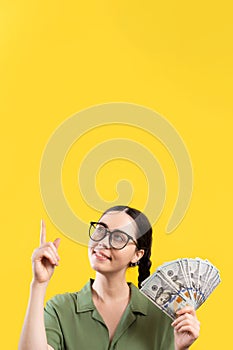 Shopping and wealth. Portrait of a smiling attractive Caucasian woman holding a fan of dollar currency and pointing up