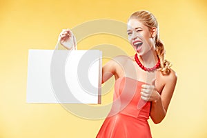Shopping. Young smiling woman showing sale bag make her thumb up in black friday holiday. Girl on yellow background with