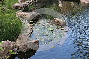 The shore of the artificial pond is lined with large stones.