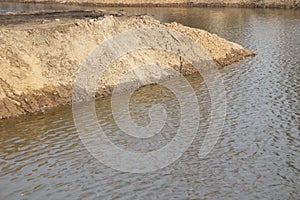 The shore of an artificial pond. A mound of sand on the water.