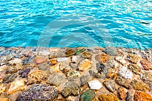 Shore of beautiful multicolored stones washed by clear blue water. Background