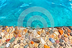 Shore of beautiful multicolored stones washed by clear blue water. Texture