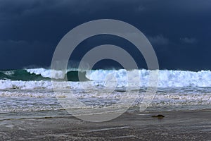 Shore breaking wave with storm on the horizon