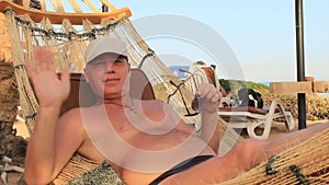 On the shore of the Kars Sea in Egypt, a young man in a sun cap rests in a hammock on a sunny summer day in the shade of palm tree