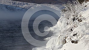 The shore of Lake Baikal covered with ice and snowstorms with snowy trees, the water soars