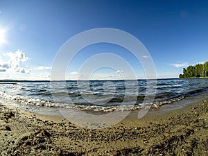 Shore of the lake, sand, lapping waves, blue sky with light clouds, fisheye lens, lake Uvildy