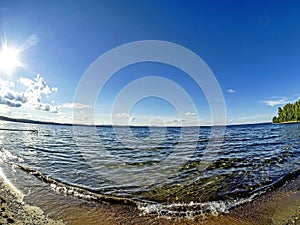 Shore of the lake, sand, lapping waves, blue sky with light clouds, fisheye lens, lake Uvildy