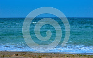Shoreline on sandy beach, watery waves on the Black Sea during a windy summer day with a blue sky