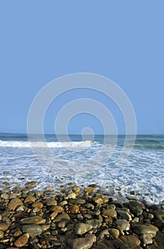 Shorline round wet rocks with crashing blue waves and sky