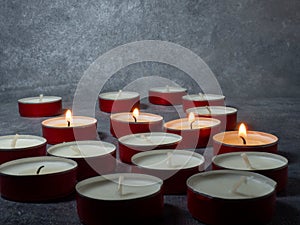 Short candles are burning against a dark background. Lots of small candles. Not all candles are lit