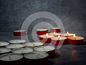 Short candles are burning against a dark background. Lots of small candles. Not all candles are lit