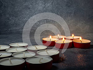 Short candles are burning on a dark background. Lots of small candles. Not all candles are lit