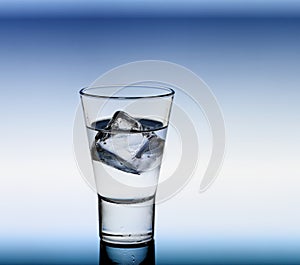 Short drink glass with clear liquid and ice cubes