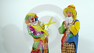 Short funny clown scares the other clown with huge scissors